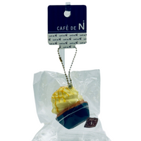 Cupcake-shaped keychain in clear packaging with a Cafe de N tag on a white background