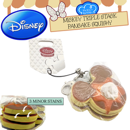 Disney Exclusive RARE Mickey Mouse Triple Stack Pancake Squishy with realistic golden-brown pancake texture, stacked in three layers with a Mickey face imprint. Includes original packaging, tag, cellphone strap, and durable clip. Slight discoloration with three mini stains visible on lower pancake layer, as indicated in the bottom-left reference image.