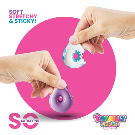 Two hands holding a purple and white toy with a pink background, featuring the Tabby Jelly Squeezy branding.